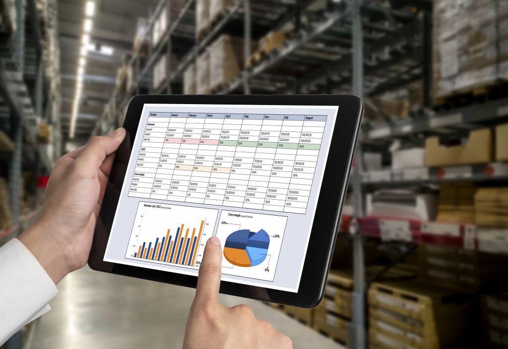 A person is holding a Tablet displaying an inventory software dashboard